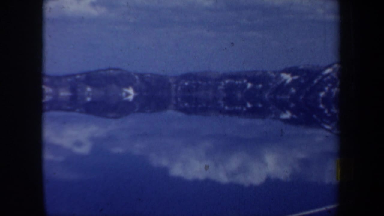 Blue-tinted mirrored mountain landscape with dark film borders and snow-like light areas.
