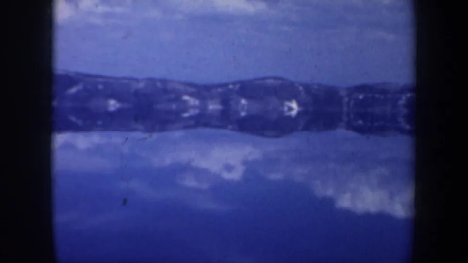 1957 Oregon home-movie frame showing a blue-toned mirrored mountain form, likely from camera or film distortion in the scanned footage.