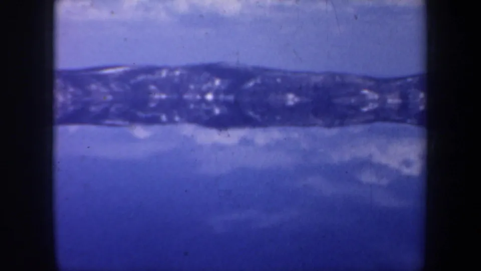 Final Oregon 8mm frame with a blue mirrored mountain band, dark gate edges, and visible grain from the original home-movie scan.