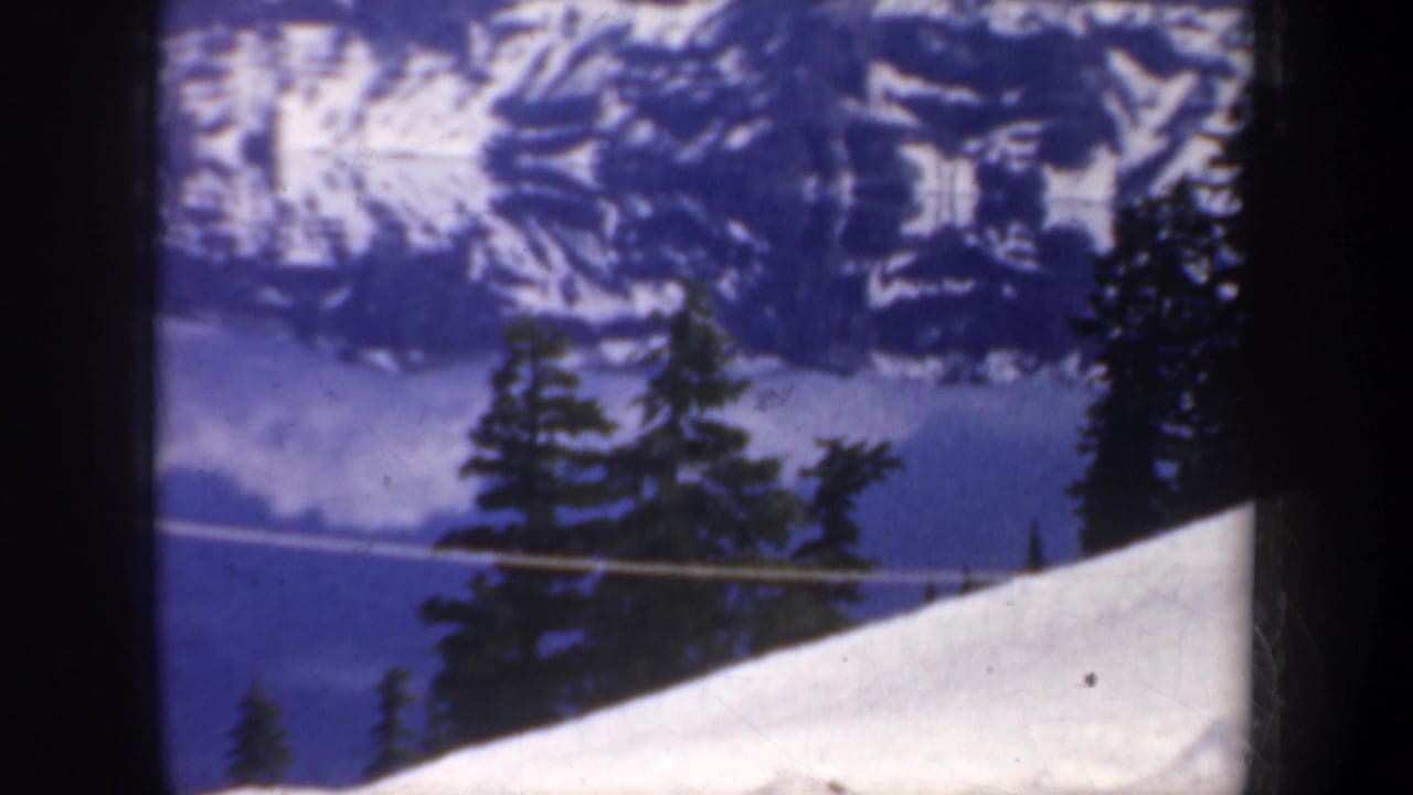 Snowy mountain and evergreen trees reflected in a blue lake.