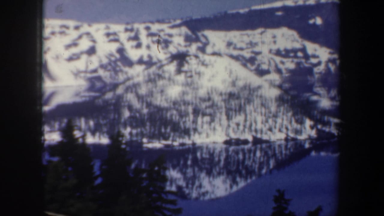 Snowy valley wall and lake reflection framed by dark foreground trees.