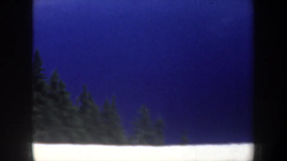 1957 Oregon 8mm frame with snow, evergreen treetops, and a deep blue lake or sky area framed by the film edge.