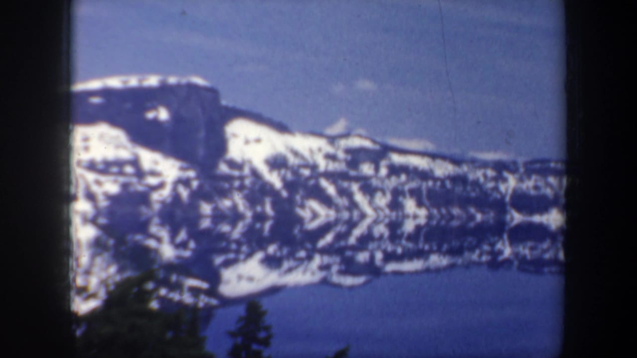 Snow-capped mountains and a lake seen through dark tree silhouettes.
