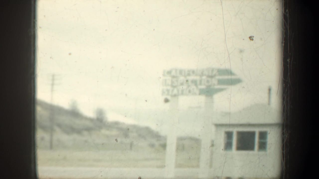 Roadside California Inspection Station sign beside a small building and hillside.