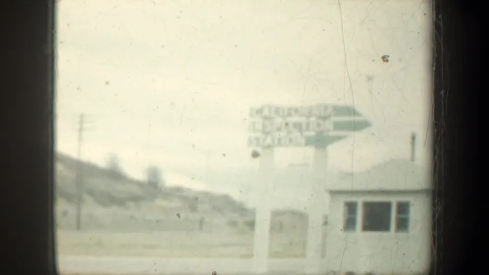 Roadside California Inspection Station sign appears near a small station building, with hills and utility poles in soft 8mm footage.