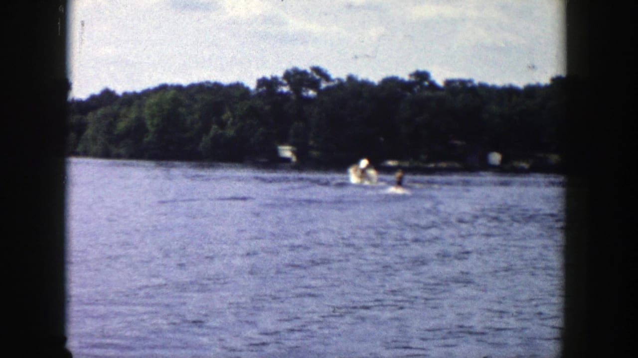 Distant boat activity on a lake near a wooded shoreline.
