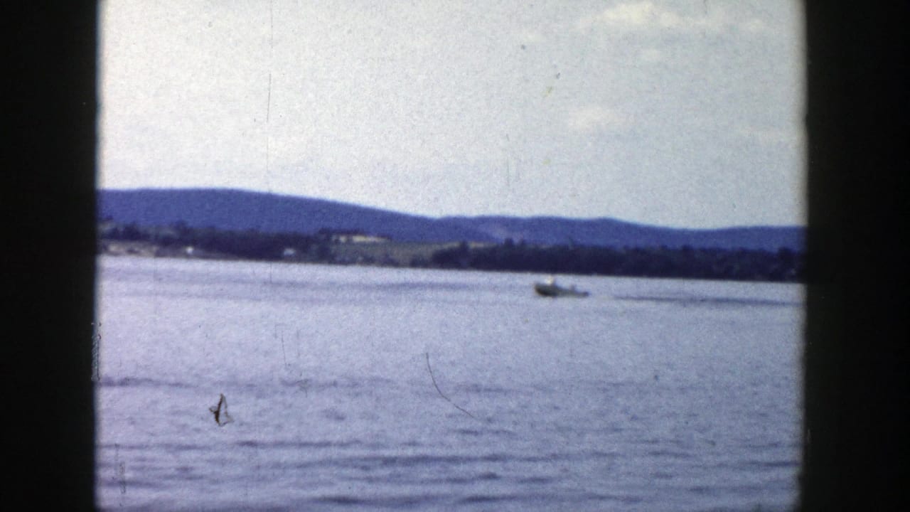 Wide 1958 Wisconsin lake frame showing a distant boat, rippled water, low shoreline hills, and aged color 8mm texture.