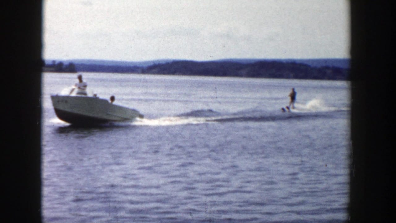 1958 Wisconsin home-movie frame of a motorboat carrying people while towing a water skier across open lake water.