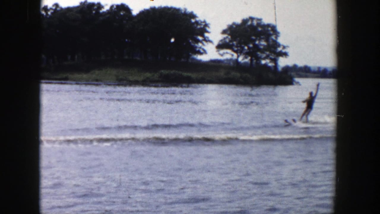 1958 Wisconsin home-movie frame of a distant man water skiing across a calm lake behind dark window framing.