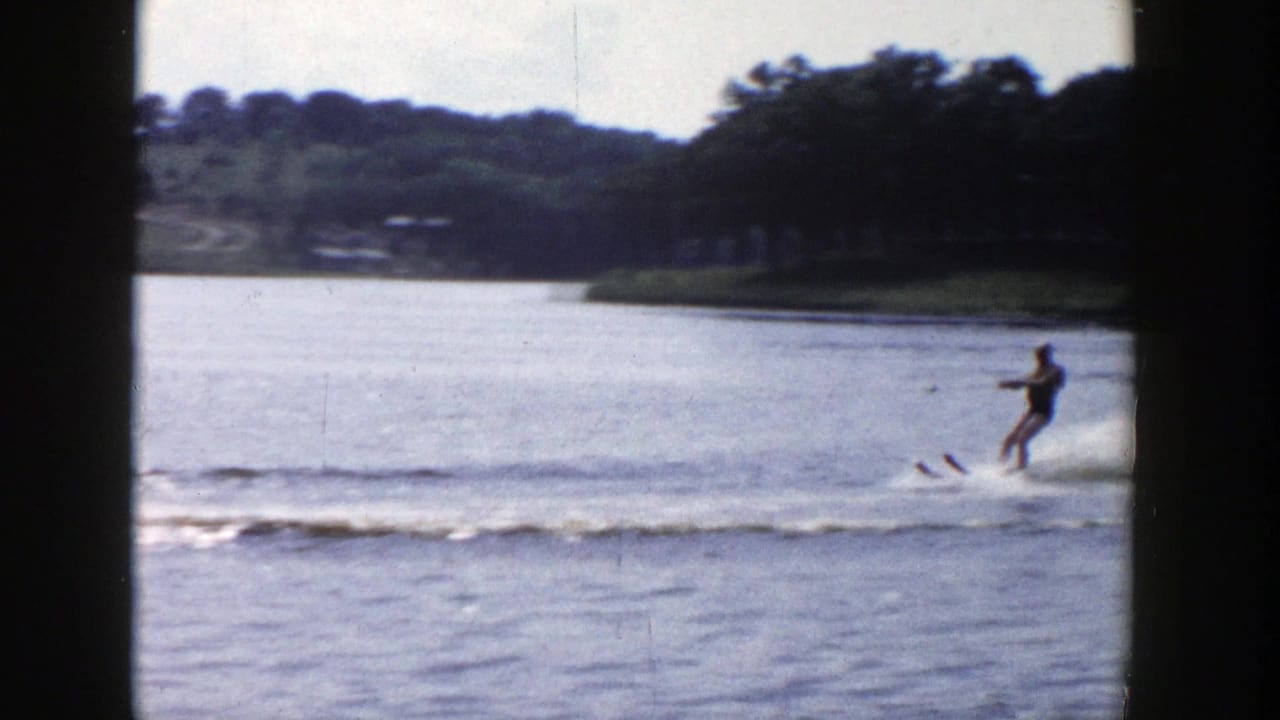 A distant water skier glides near the right edge of a Wisconsin lake scene, with wooded banks and houses beyond.