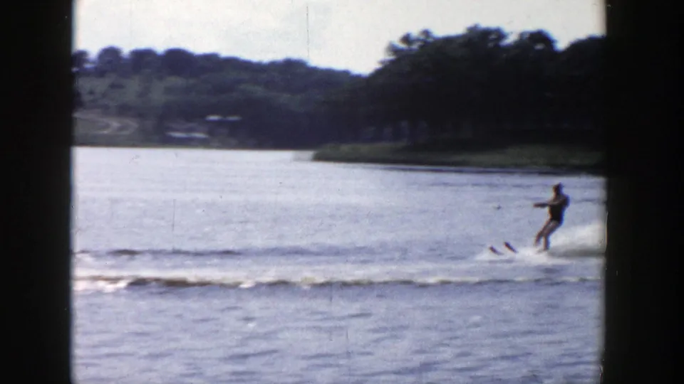 A distant water skier glides near the right edge of a Wisconsin lake scene, with wooded banks and houses beyond.
