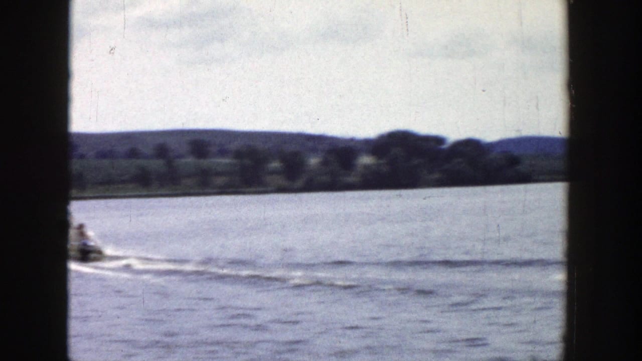 1958 Wisconsin 8mm frame showing a small motorboat moving across a lake near a tree-lined shore.