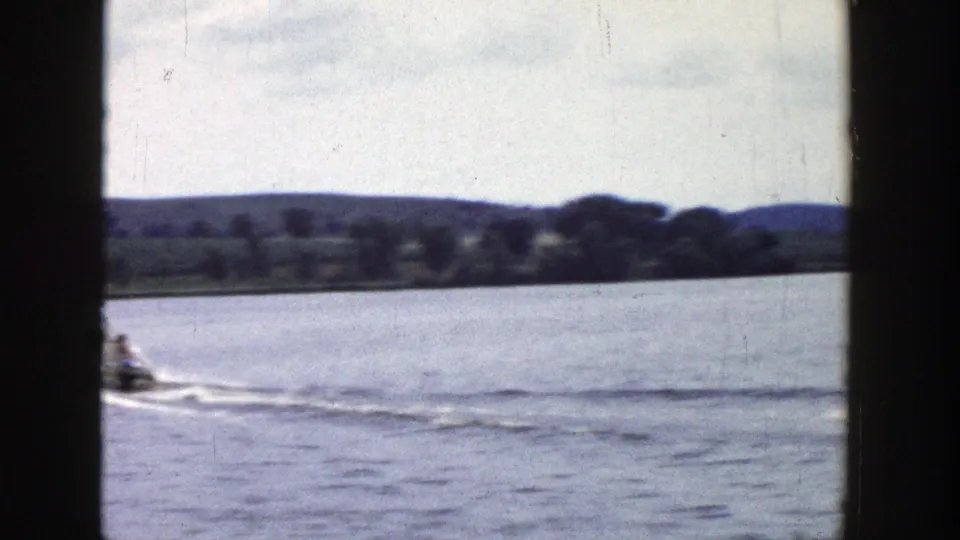 1958 Wisconsin 8mm frame showing a small motorboat moving across a lake near a tree-lined shore.