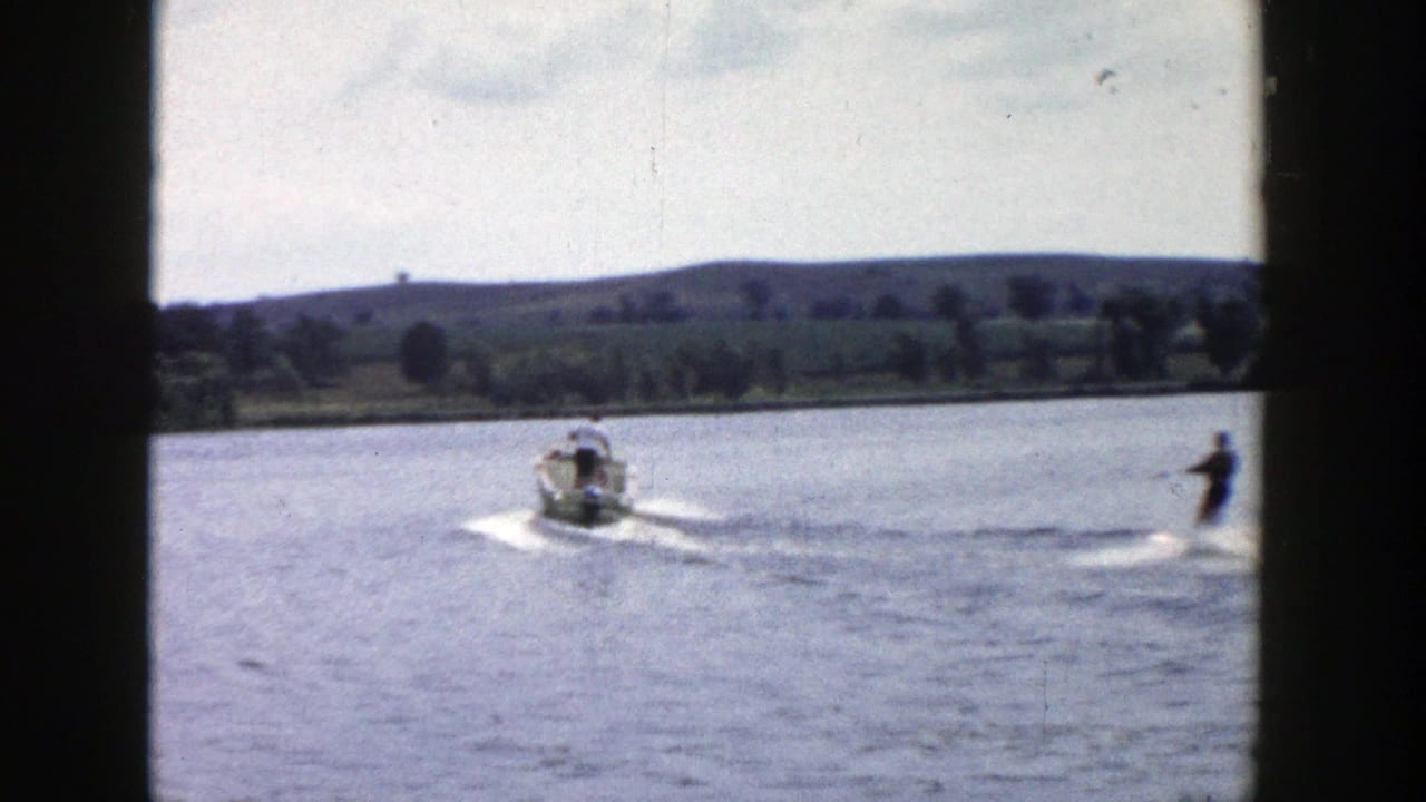 1958 Wisconsin lake scene with a motorboat pulling a distant water skier across the frame.
