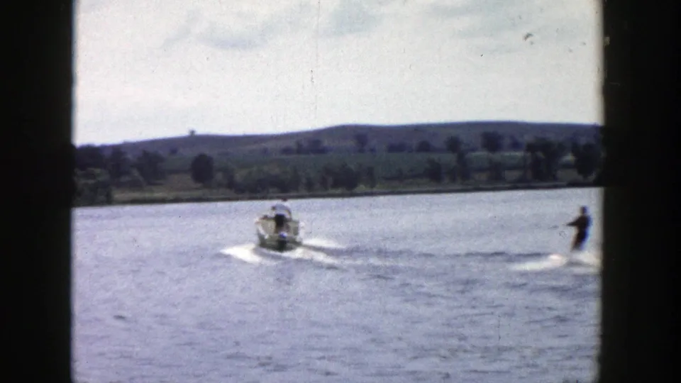1958 Wisconsin lake scene with a motorboat pulling a distant water skier across the frame.