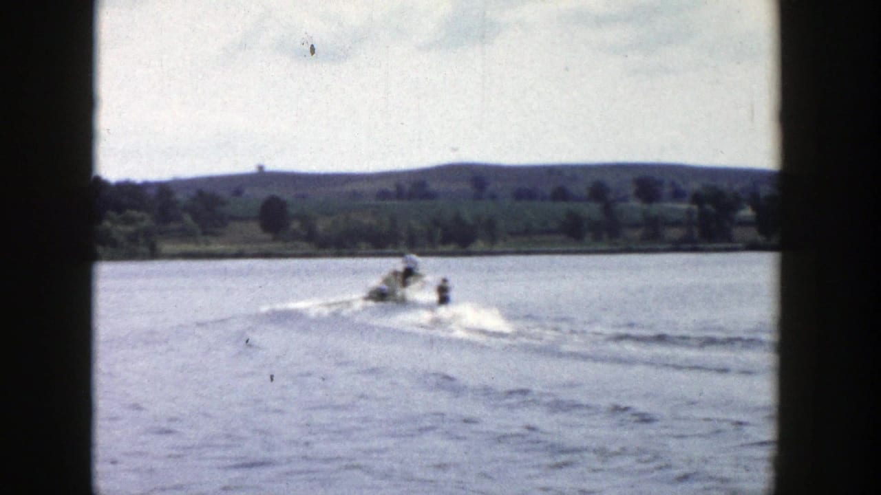 1958 Wisconsin 8mm frame showing a boat and skier farther from the camera on a sunny lake.