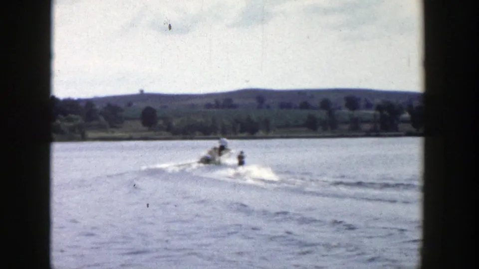 1958 Wisconsin 8mm frame showing a boat and skier farther from the camera on a sunny lake.