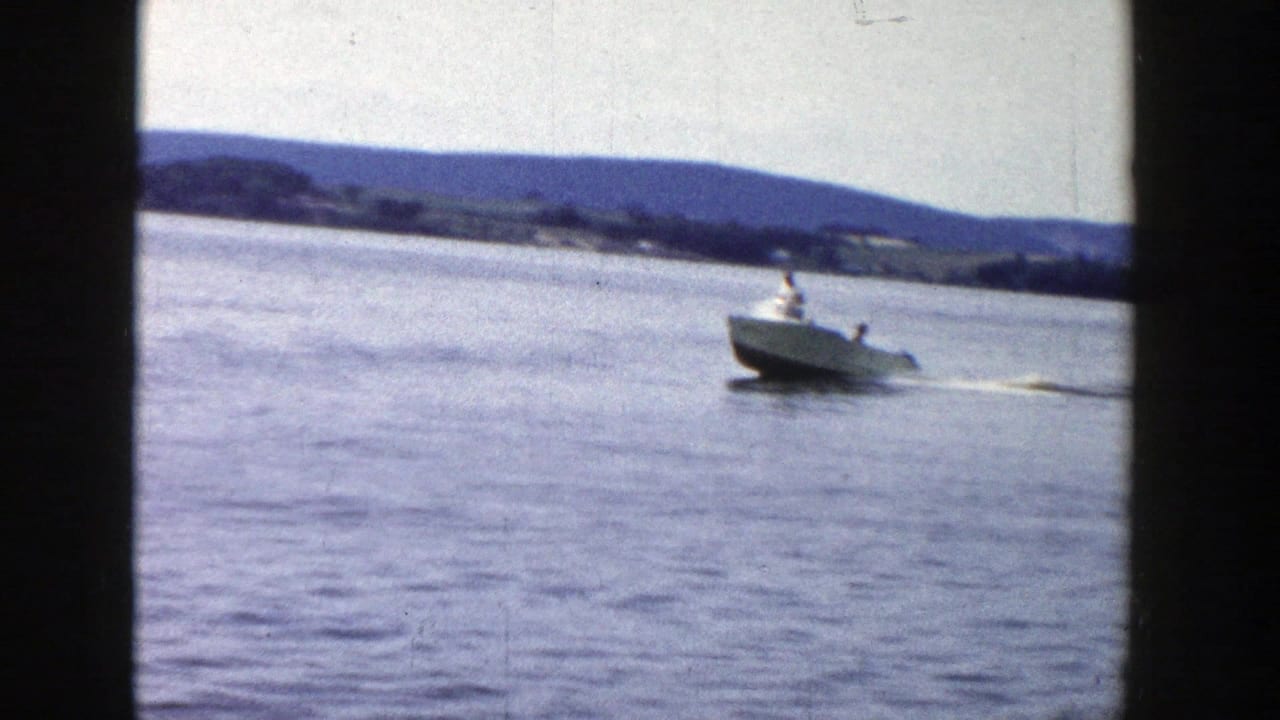 Motorboat crossing a lake with a water skier starting behind it near a distant shoreline.