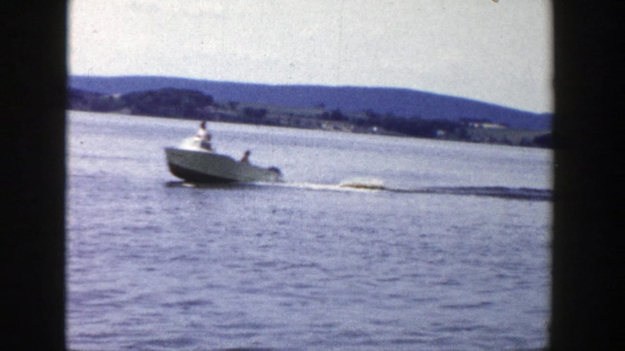 The boat speeds across a Wisconsin lake in 1958 home-movie footage, towing a distant water skier through a white wake.