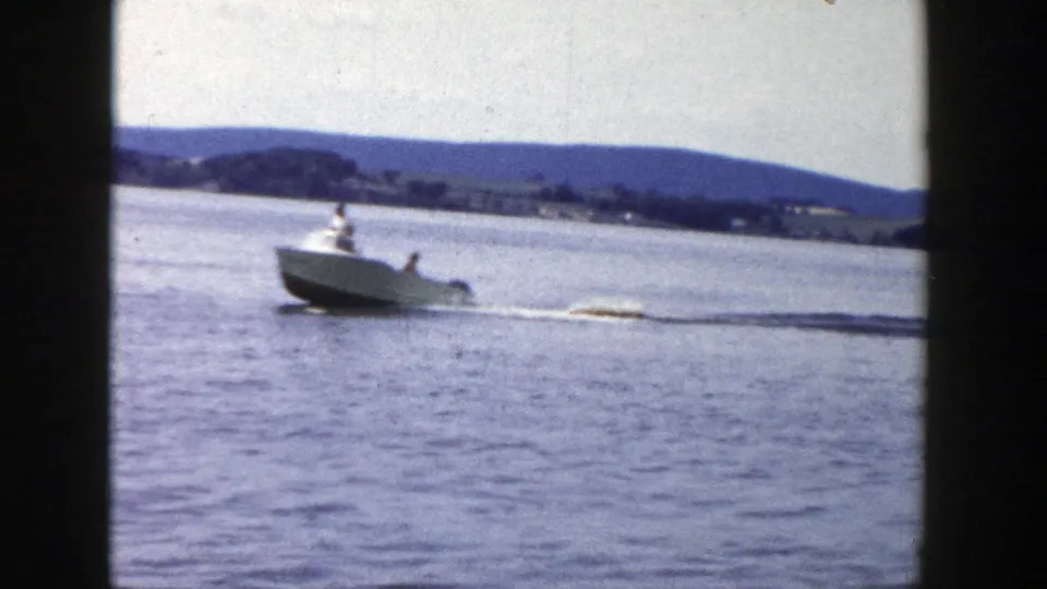The boat speeds across a Wisconsin lake in 1958 home-movie footage, towing a distant water skier through a white wake.