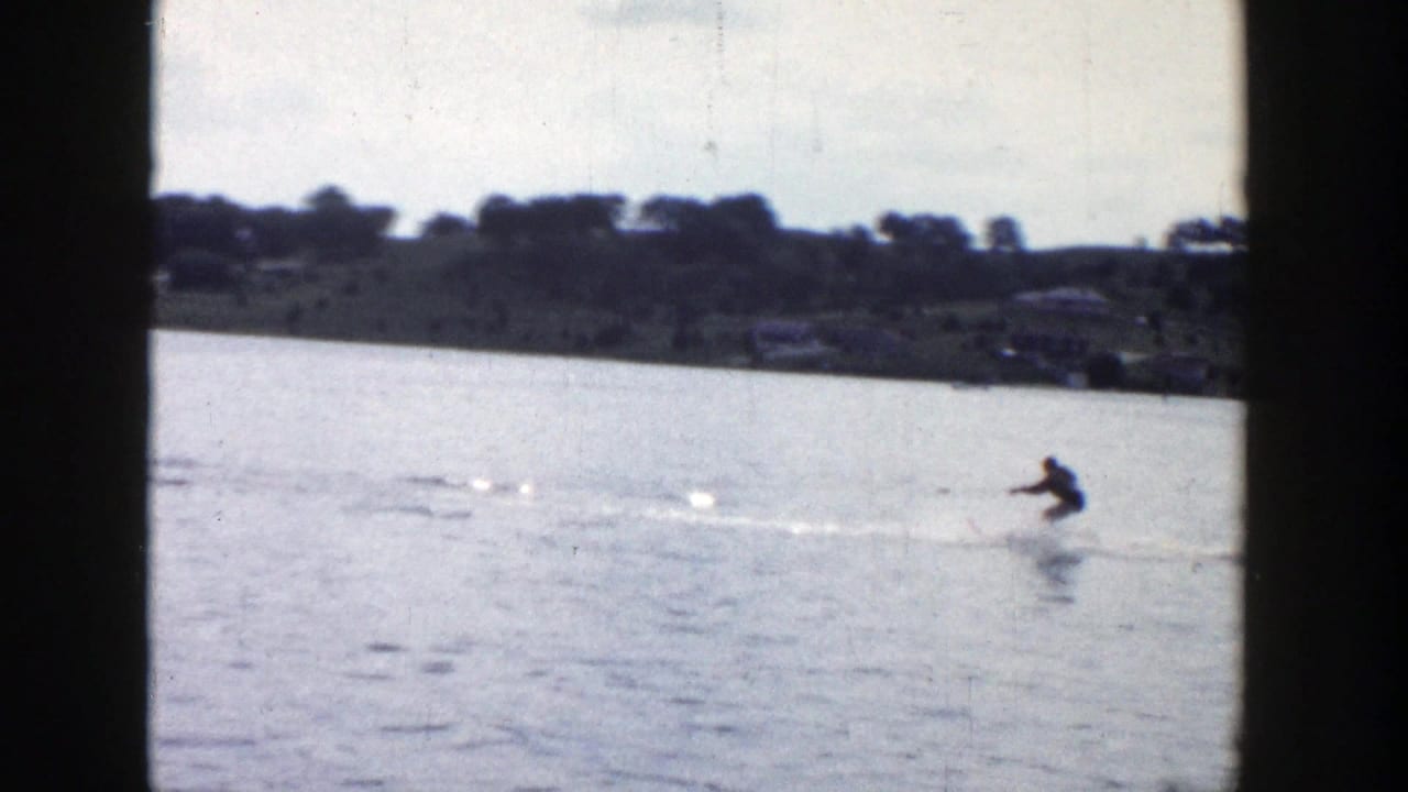 A distant skier in 1958 Wisconsin footage leans across the water while a white wake cuts over the lake surface.