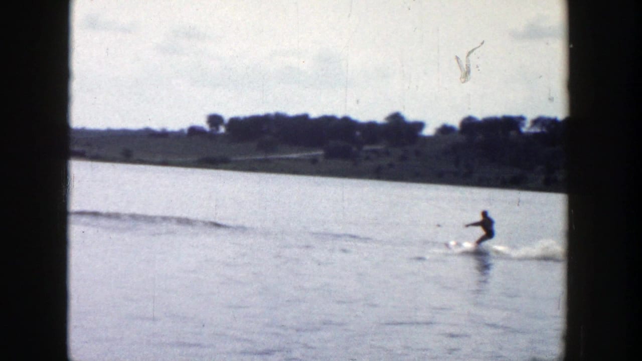 The 8mm frame shows a skier skimming over a Wisconsin lake, with a low wooded shoreline and soft sky in the background.
