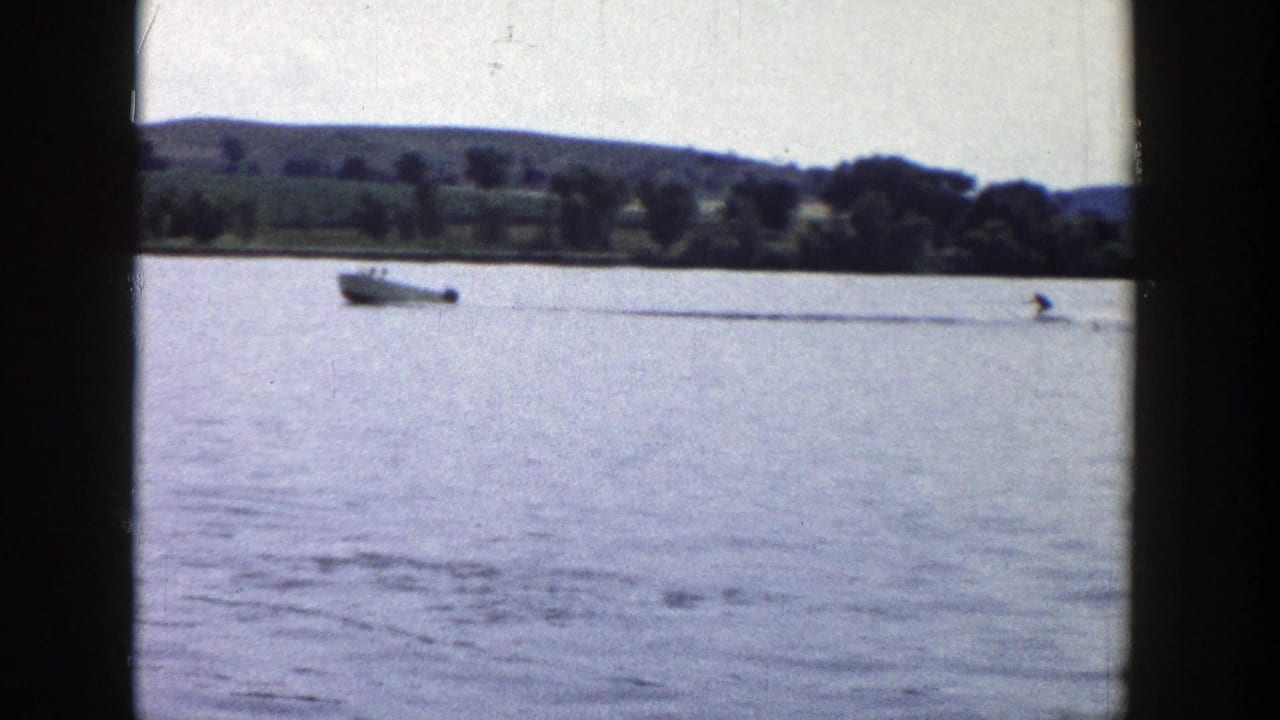 The motorboat and rope-towed rider continue across the lake in a faded 8mm home-movie view of rural Wisconsin recreation.