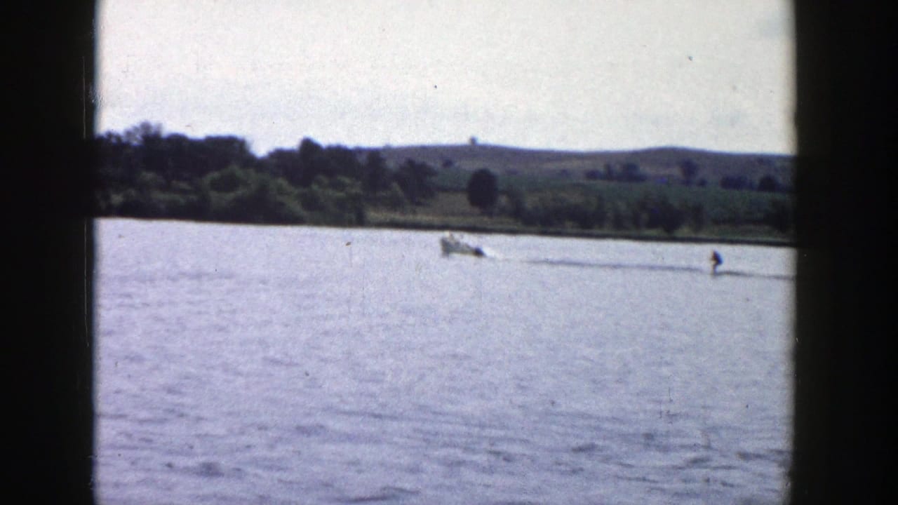 The boat and skier move farther across a Wisconsin lake, framed by dark 8mm gate edges and a rural horizon.