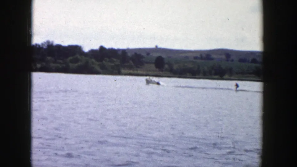 The boat and skier move farther across a Wisconsin lake, framed by dark 8mm gate edges and a rural horizon.