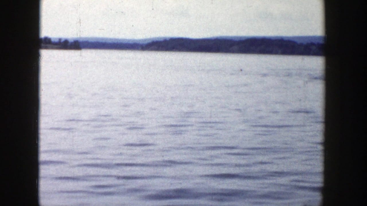 A wide 1958 Wisconsin lake view shows rippled water, a distant wooded shoreline, and low hills in faded 8mm color.