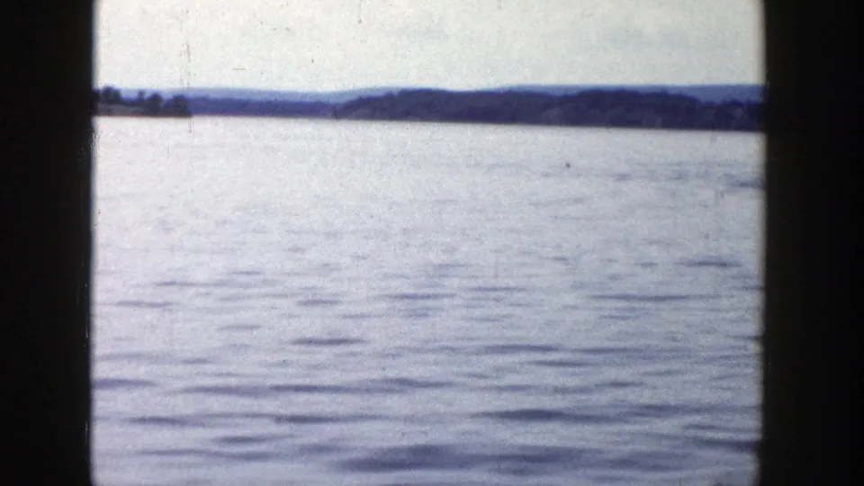 A wide 1958 Wisconsin lake view shows rippled water, a distant wooded shoreline, and low hills in faded 8mm color.