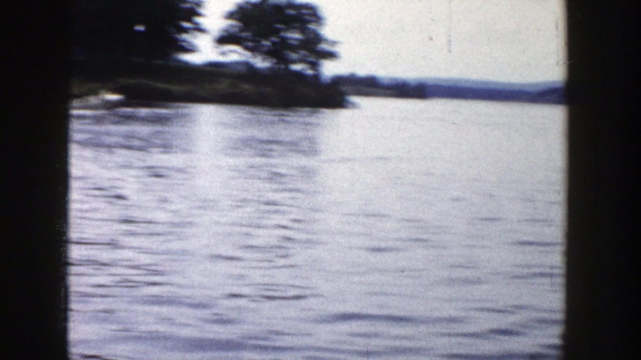 1958 Wisconsin 8mm lake view with rippled water, distant wooded shoreline, and dark vertical frame edges.