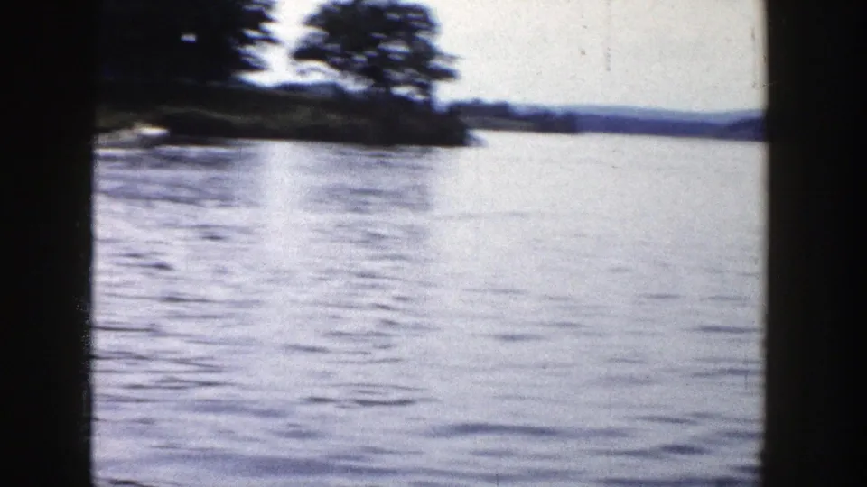 1958 Wisconsin 8mm lake view with rippled water, distant wooded shoreline, and dark vertical frame edges.