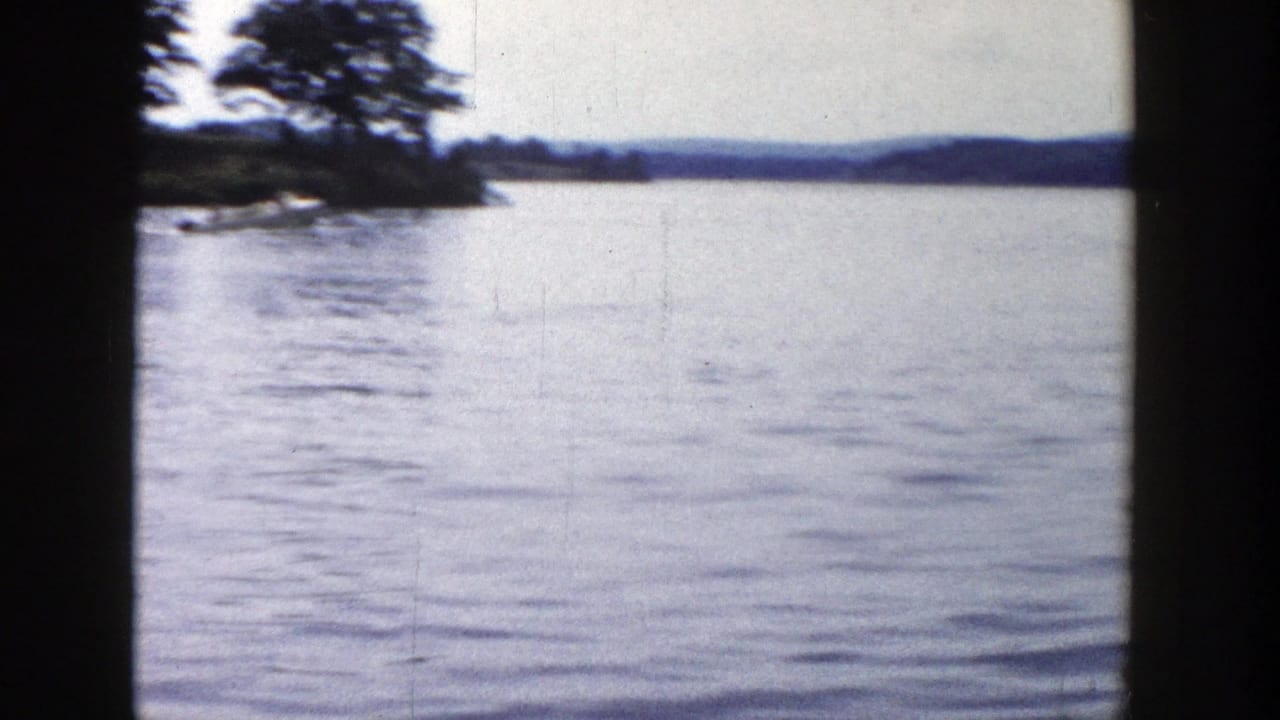 1958 Wisconsin lake scene with open water, a tree-covered point at left, and low hills on the far horizon.