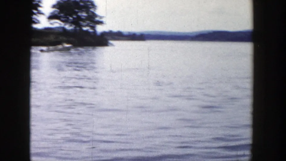 1958 Wisconsin lake scene with open water, a tree-covered point at left, and low hills on the far horizon.