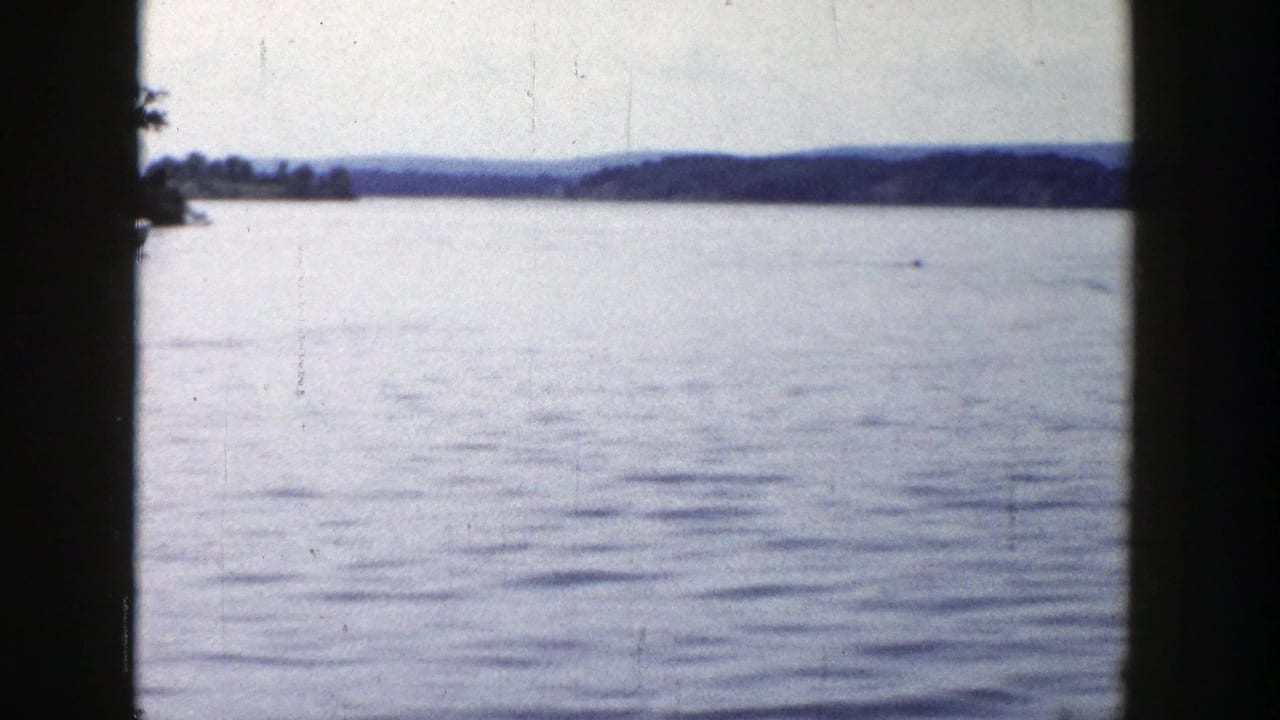 Soft 8mm view of a Wisconsin lake in 1958, showing open water, far shoreline, and low wooded hills.