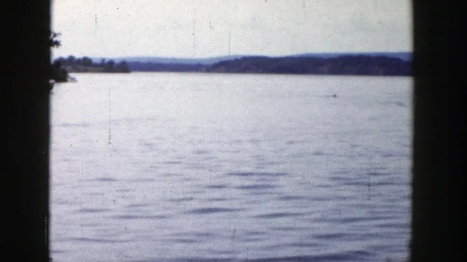 Soft 8mm view of a Wisconsin lake in 1958, showing open water, far shoreline, and low wooded hills.