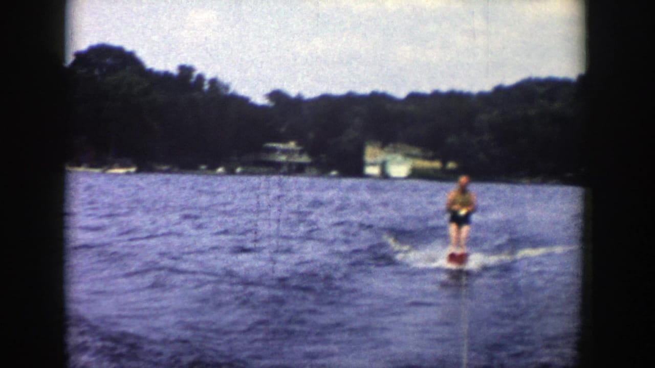 1958 Wisconsin lake footage shows the skier continuing across blue water, with a tow rope trailing back toward the camera position.