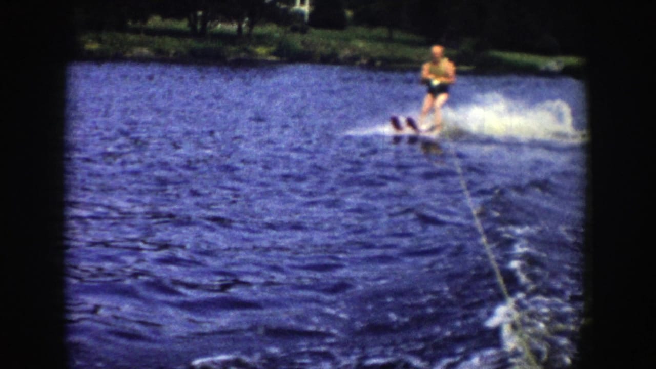 Man water skiing behind a boat on a lake with tow rope and wooded shoreline visible.