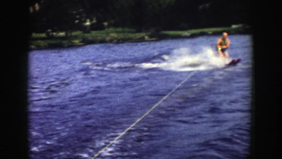 The 1958 Wisconsin lake footage shows the man water skiing closer to frame center, leaning over choppy water with spray behind him.