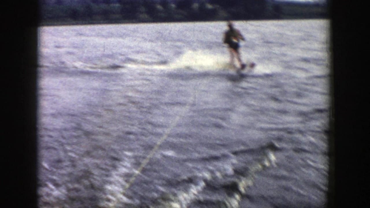 The skier crosses the water at speed, creating spray and a white wake in soft, grainy 1958 Wisconsin 8mm footage.