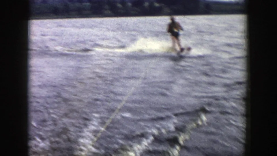 The skier crosses the water at speed, creating spray and a white wake in soft, grainy 1958 Wisconsin 8mm footage.