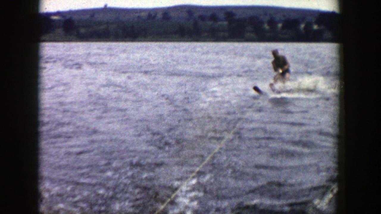 Water skier trails behind a boat on a lake with a tow rope and distant shoreline.