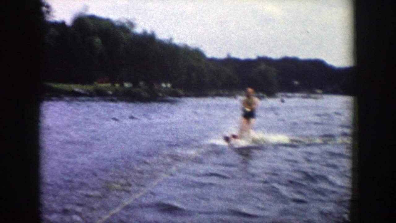 1958 Wisconsin 8mm frame showing a water skier approaching over choppy lake water, with a tow rope in the foreground and trees along the shore.