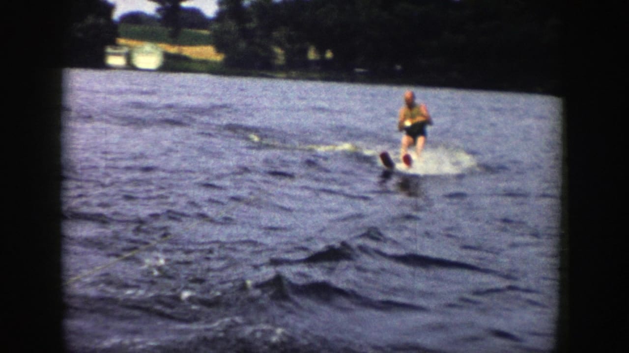 Near the end of the 1958 Wisconsin clip, the skier continues over choppy water with trees and small shoreline structures beyond.