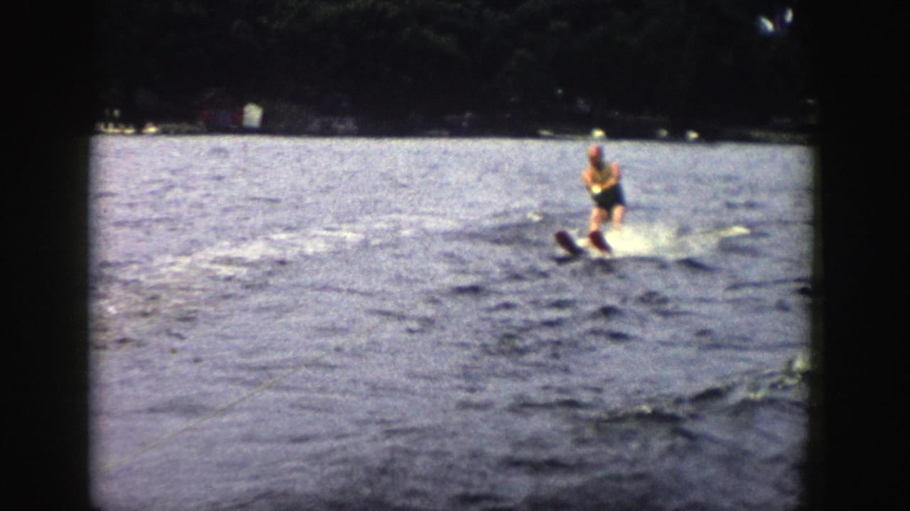 A man in a yellow life vest balances on water skis in a 1958 Wisconsin home-movie view from a moving boat.