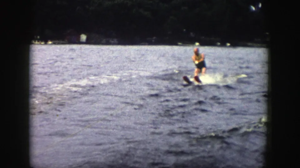A man in a yellow life vest balances on water skis in a 1958 Wisconsin home-movie view from a moving boat.