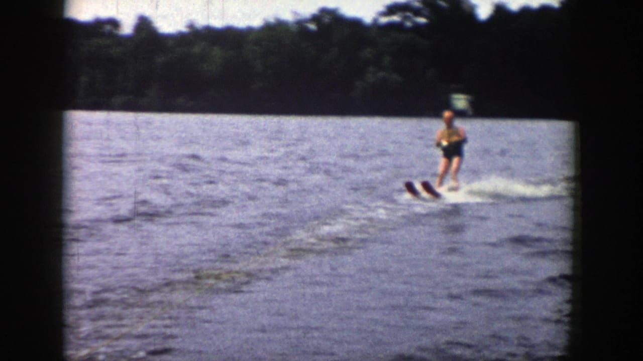Young person water skiing on a Wisconsin lake in 1958, seen in soft 8mm color with wooded shoreline behind.