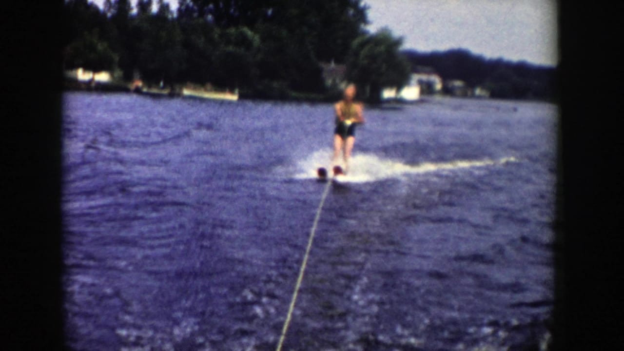 The skier rides behind a visible tow rope on a Wisconsin lake, with trees and small distant shoreline buildings behind.