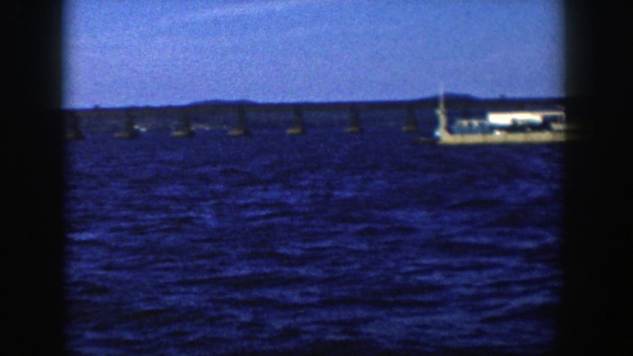 1958 Wisconsin 8mm frame with a white vessel near the right side, a low bridge behind it and choppy blue water in the foreground.
